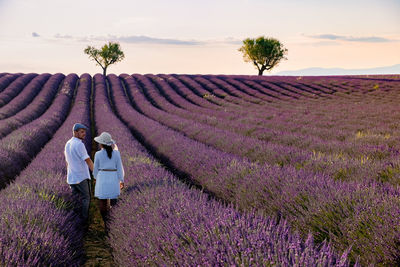 Rear view of couple standing on flowering field against sky