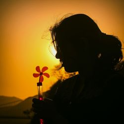 Close-up of silhouette woman holding pinwheel toy against clear orange sky