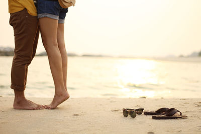 Low section of couple standing at shore of beach