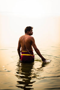 Rear view of shirtless man in sea against sky