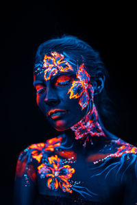 Young woman with paint on her body against black background