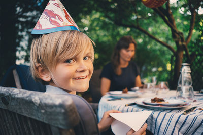 Portrait of happy boy wearing hat while holding tissue paper at garden dinner party