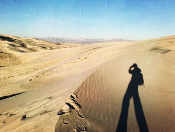 Shadow of man on sand dune in desert against clear sky