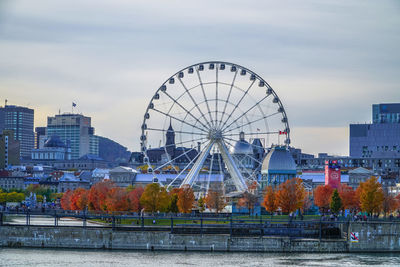 Ferris wheel by river against sky in city