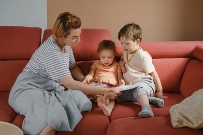 Mother reading book with two kids on sofa. happy family moments at home. spending time and educating