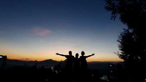 Silhouette people standing by tree against sky during sunset