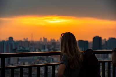 Rear view of woman looking at cityscape during sunset