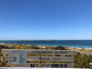 Information sign by sea against clear blue sky