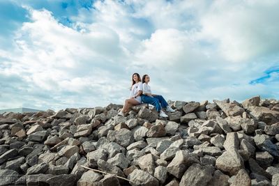 Woman sitting on rock against sky