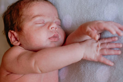 Calm cute infant with closed eyes covered with blanket resting in bed against blurred interior of light bedroom