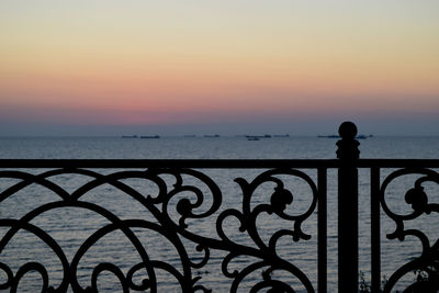 Silhouette railing by sea against sky during sunset