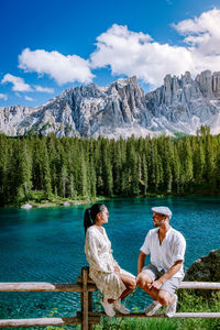 Rear view of couple sitting on mountain against sky