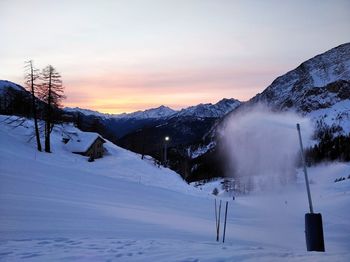 Snow covered landscape against sky during sunset