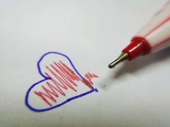 Cropped image of pen by heart shape with pattern on paper