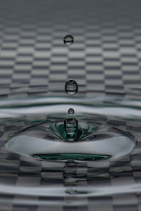 Close-up of drop splashing in water with chess pattern in the background