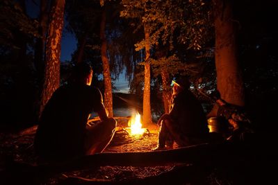 Friends sitting by campfire in forest at night