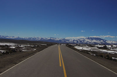 Straight road leading towards mountain against sky