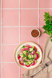 Healthy vegan salad with watermelon radish, cucumber and red onion on pink tile background