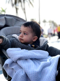 Little boy in his baby carriage, looking around, serious, on a winter day with a blanket on her lap. 