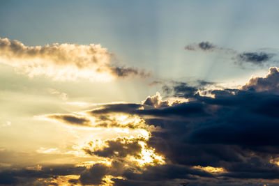 Low angle view of sunlight streaming through clouds during sunset