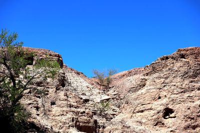 Low angle view of rocky mountains against clear blue sky