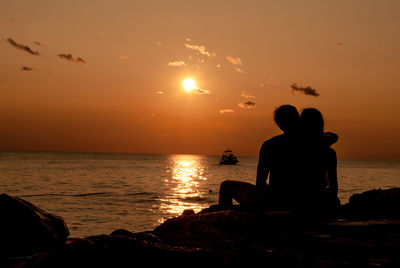 Silhouette affectionate couple sitting at beach during sunset