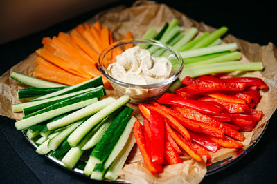 Vegetables cut into strips cucumber, red bell pepper, carrots, celery and hummus in a glass bowl.