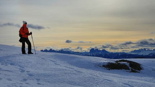 Hiker lady contemplating dolomite mountain range standing atop a snow covered peak 