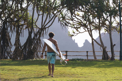 Young man walking and carrying surfboard