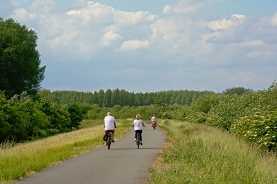 Rear view of people riding bicycle on road against sky