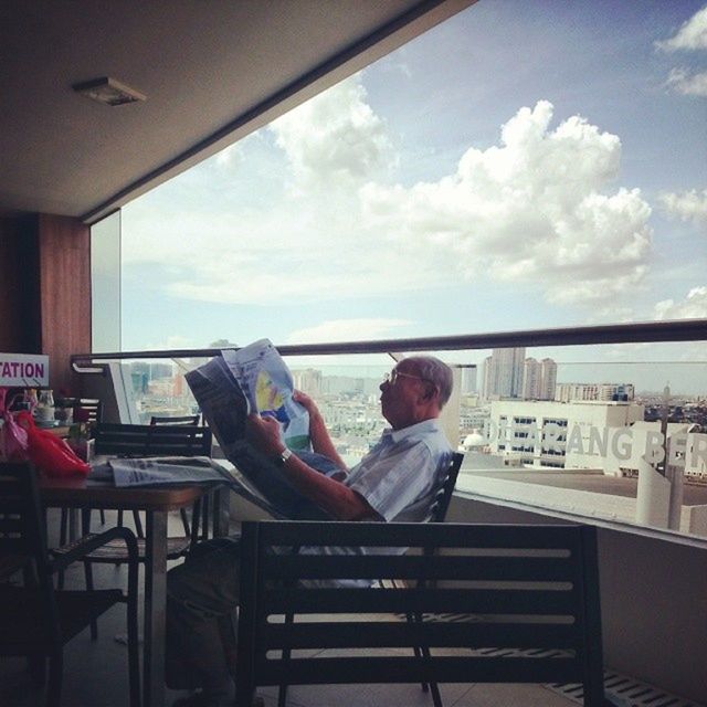 sitting, lifestyles, leisure activity, relaxation, sky, indoors, casual clothing, rear view, chair, built structure, men, architecture, full length, railing, cloud - sky, person, togetherness