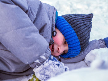 Cute boy lying on snow covered land during winter