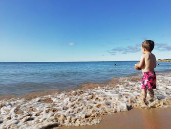 Full length of shirtless boy on beach against sky