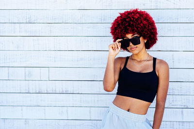 Young woman using phone while standing against wall