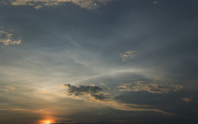 Low angle view of sunlight streaming through clouds during sunset