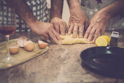 Midsection of male friends kneading dough on kitchen island