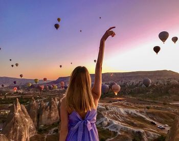 Rear view of woman against hot air balloons in sky during sunset