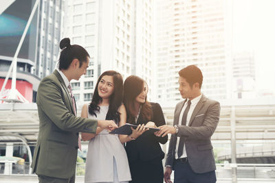 Smiling colleagues analyzing data while standing against buildings in city