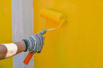 Midsection of woman holding umbrella against yellow wall