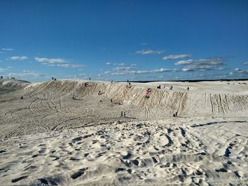 Tire tracks on sand at beach against blue sky