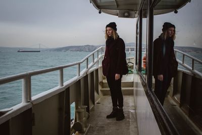 Full length of young woman standing by railing in ship