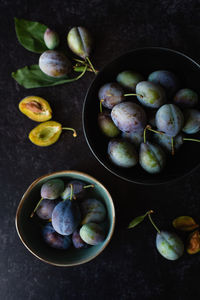 Overhead shot of bowls of fresh plums against a black background.