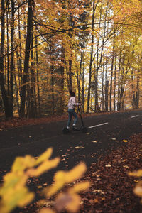 Full length of woman on push scooter in forest during autumn