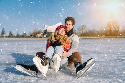 Couple wearing skaters sitting on frozen lake