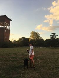 Full length of man standing with dog against sky during sunset