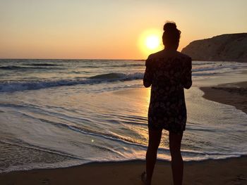 Rear view of silhouette woman standing on beach at sunset