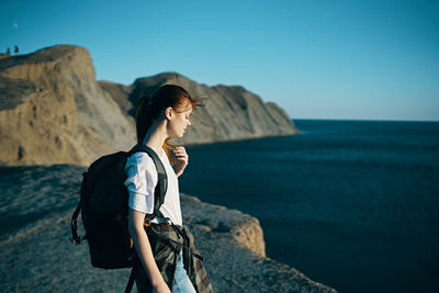 Woman standing on rock by sea against clear sky