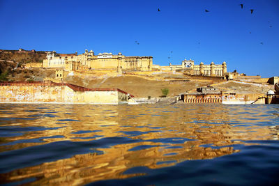 Amer fort by river against clear blue sky
