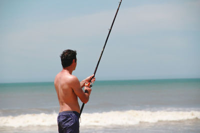 Man fishing at beach against sky