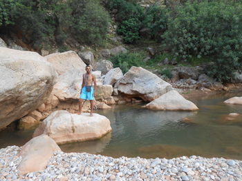 Shirtless man standing on rock at lake